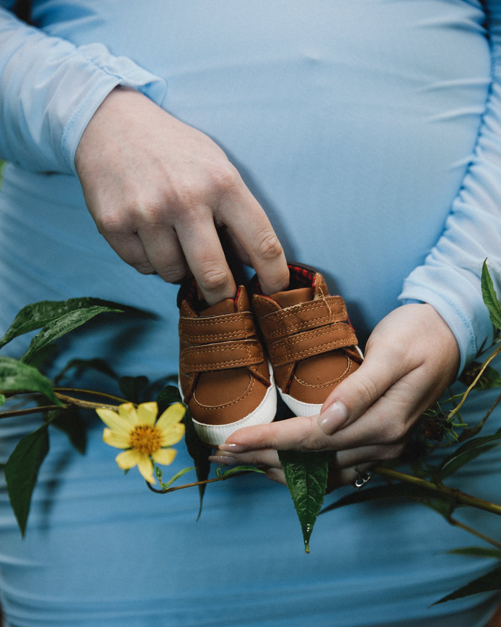 Hands holding baby shoes among flowers