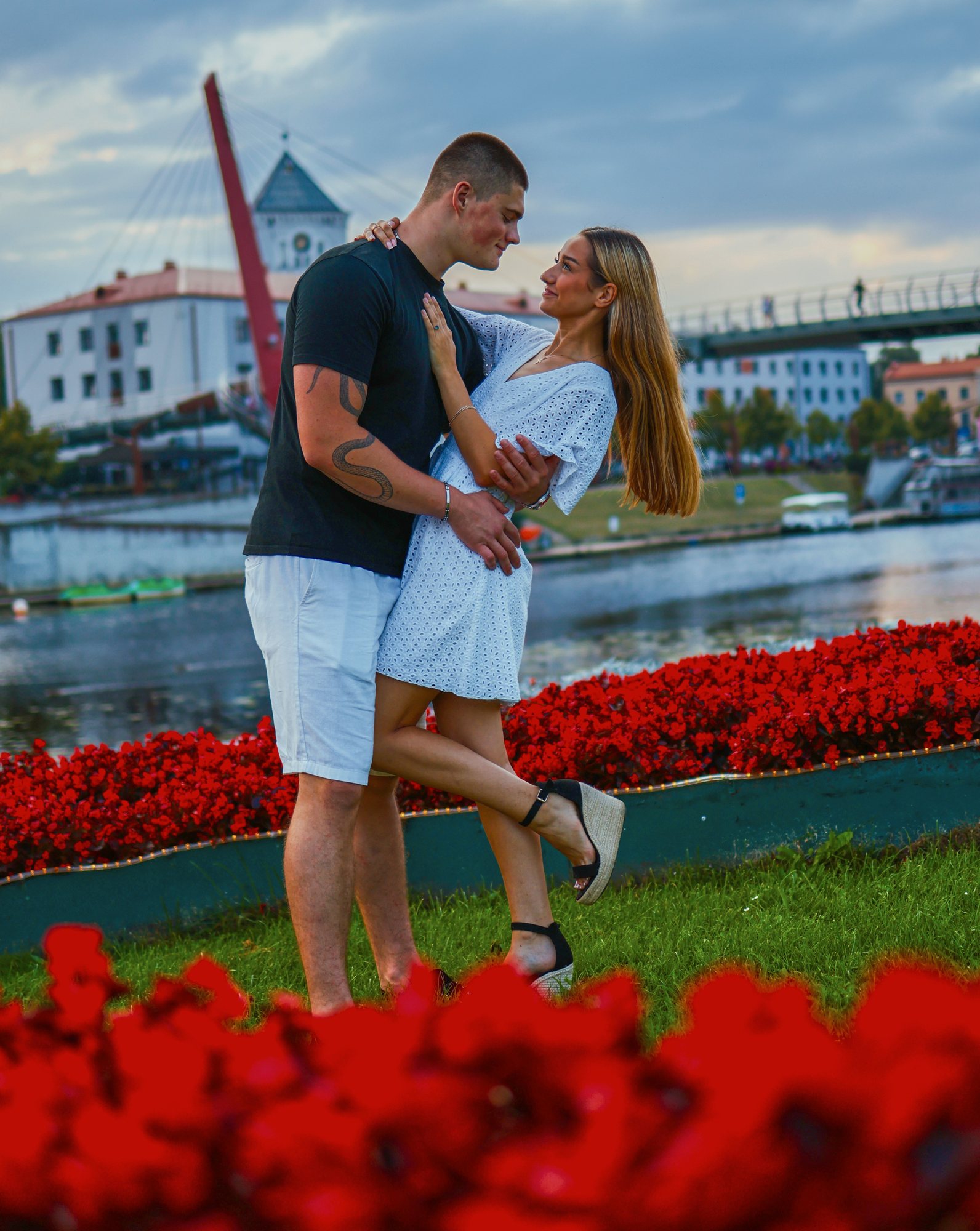 Couple embracing by the river with a bridge and red flowers, destination portrait