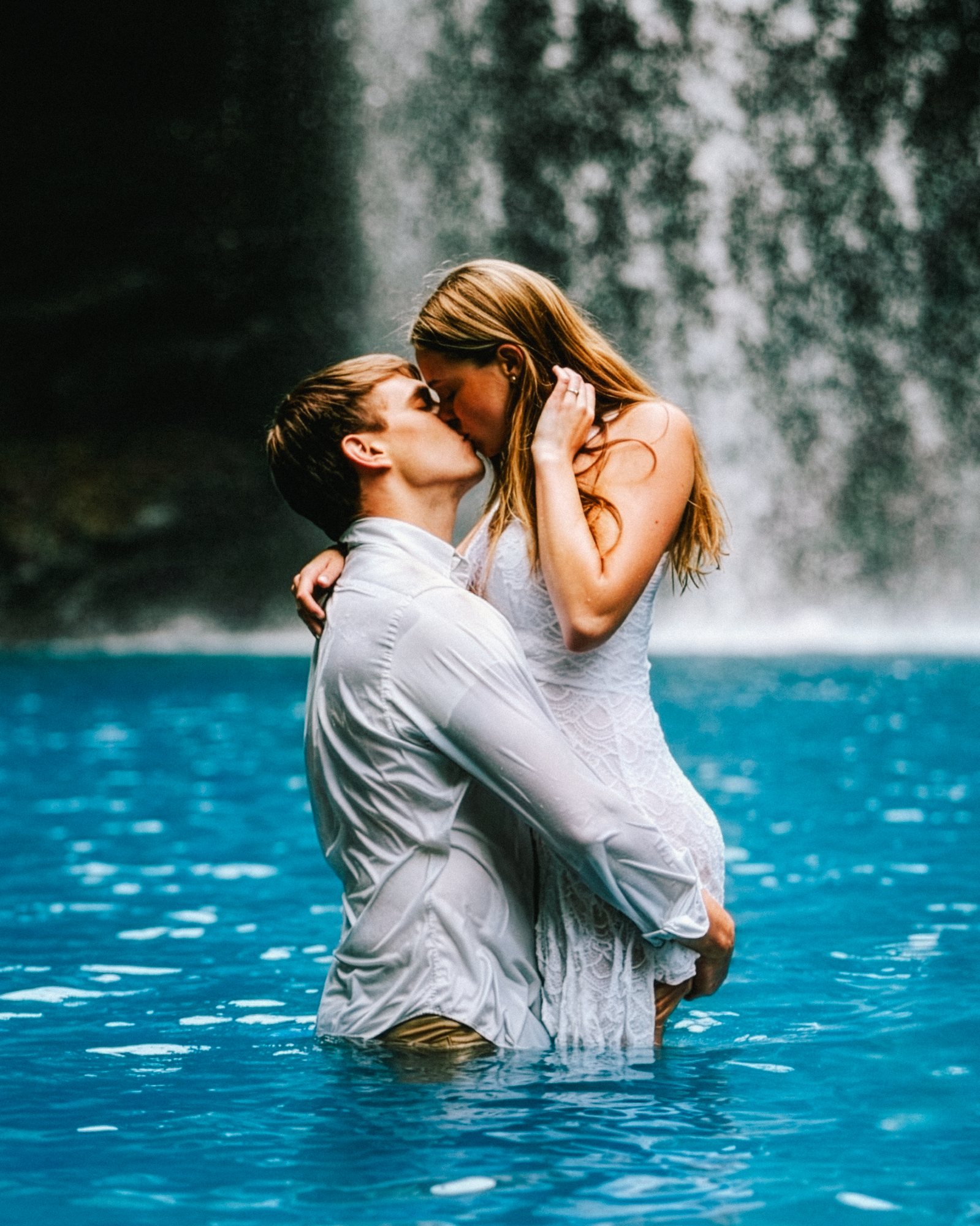 Couple kissing in a tropical waterfall lagoon, honeymoon portrait
